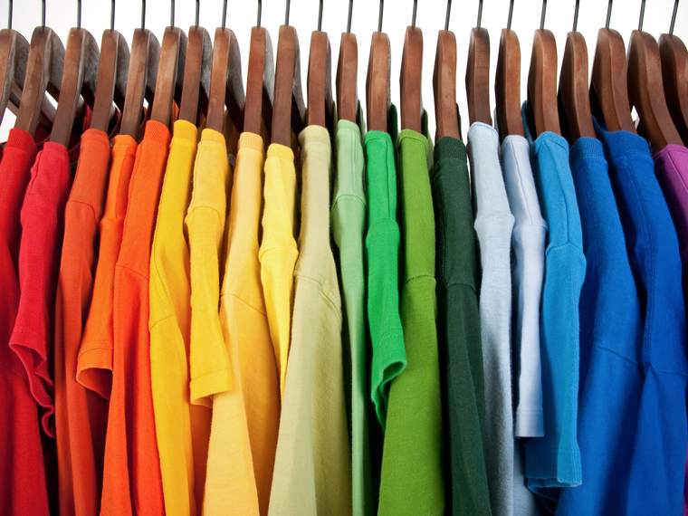 A rail of t-shirts on wooden hangers, arranged across the full range of colours.
