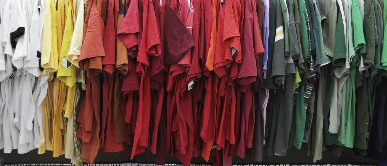 Long rails of donated shirts sorted by colour, from white through red to green.