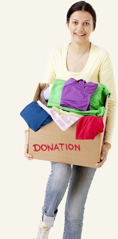 A woman carries a cardboard box marked DONATION, filled with folded clothing.