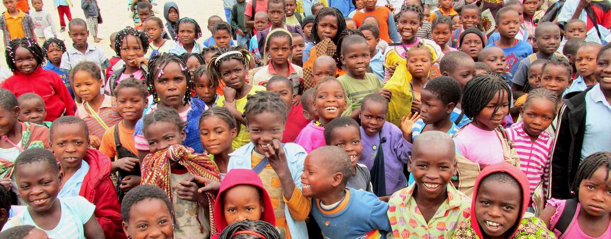 A large group of schoolchildren gathered in a schoolyard, smiling at the camera