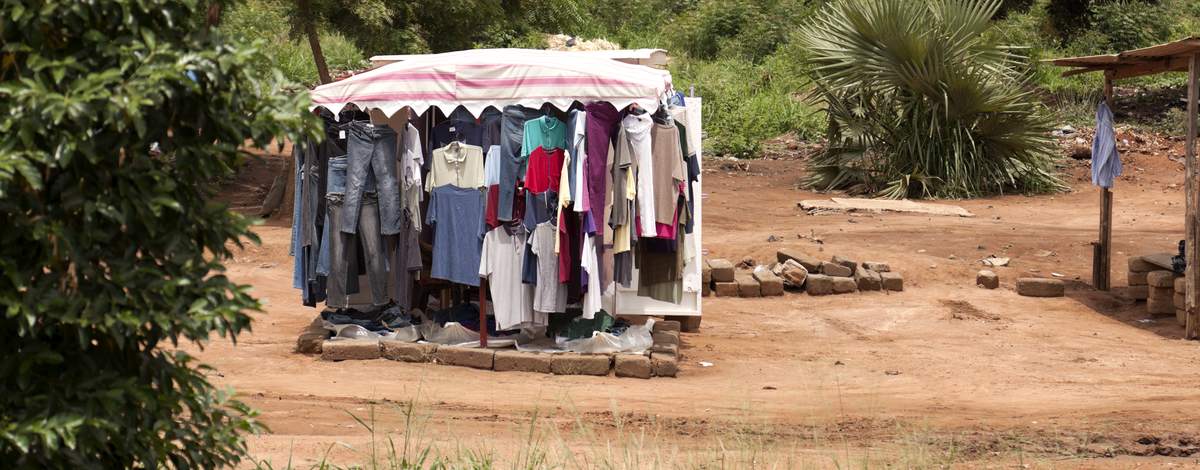 A roadside secondhand clothing stall with jeans and shirts hung under an awning