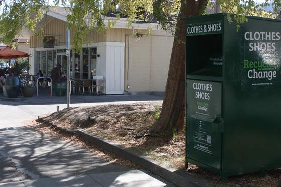 A dark green Recycle for Change clothes and shoes collection box standing beneath a tree on a residential street.