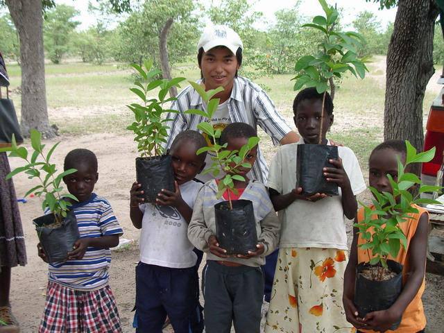 Five children hold tree seedlings in planting bags, standing with a volunteer.